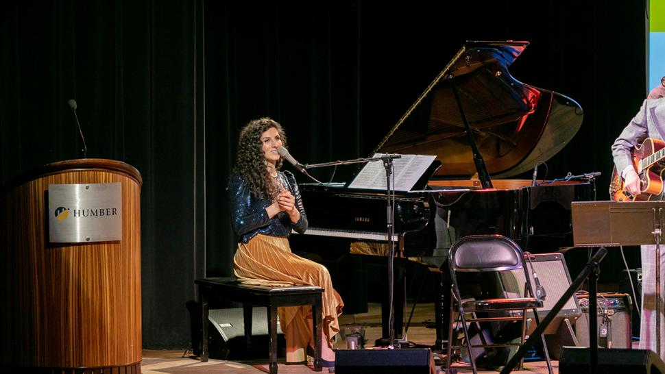 A person sits at a piano and speaks into a microphone.