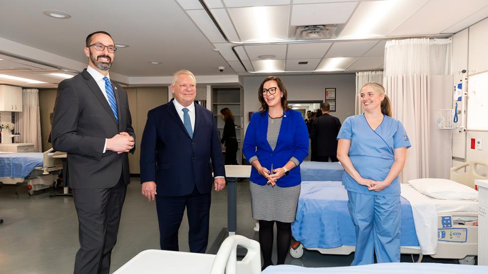 Three smiling people stand next to another person wearing medical scrubs.