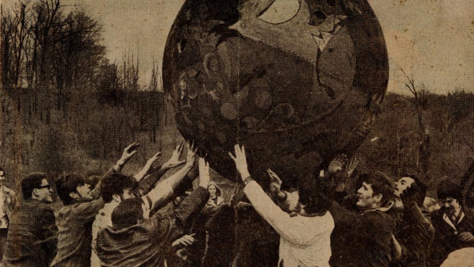 Humber students play Monsterball in April 1970. It’s believed the team in the darker clothing may be the North Campus team while the players in the lighter-coloured clothing may be the Lakeshore (Queensway) campus team. A large group of people use their hands to hold up a large ball with a face painted on it in a black and white photo.