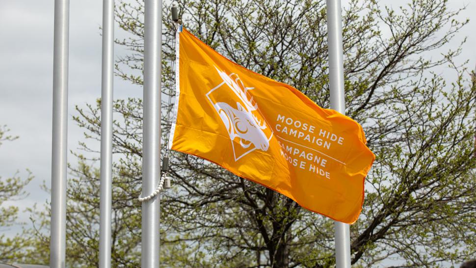 An orange flag with the words Moose Hide Campaign written on it flies from a flagpole.