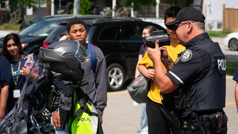 Youth had a chance to explore possible future careers in emergency response when Humber Polytechnic hosted the Humber Motorola Solutions Foundation First Responders Camp. A police officer holds up a speed camera as youth look on.