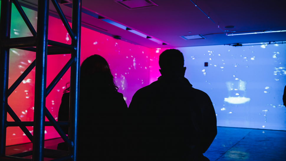 Two people look at varying colours and shapes being projected on walls.