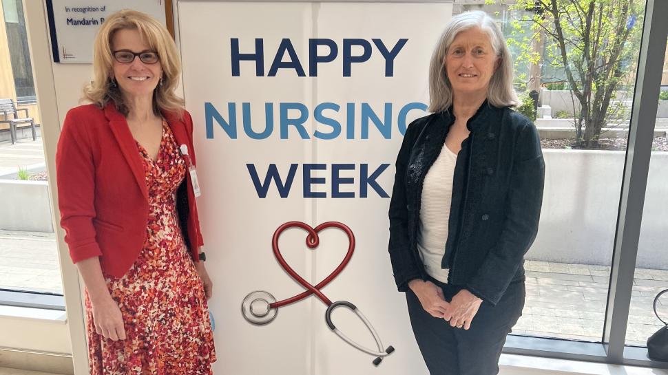 Two people stand beside a poster that reads Happy Nursing Week.