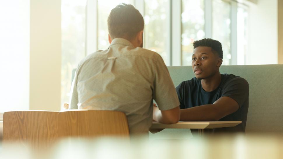 Two people sit across from each other at a table while they have a discussion. 