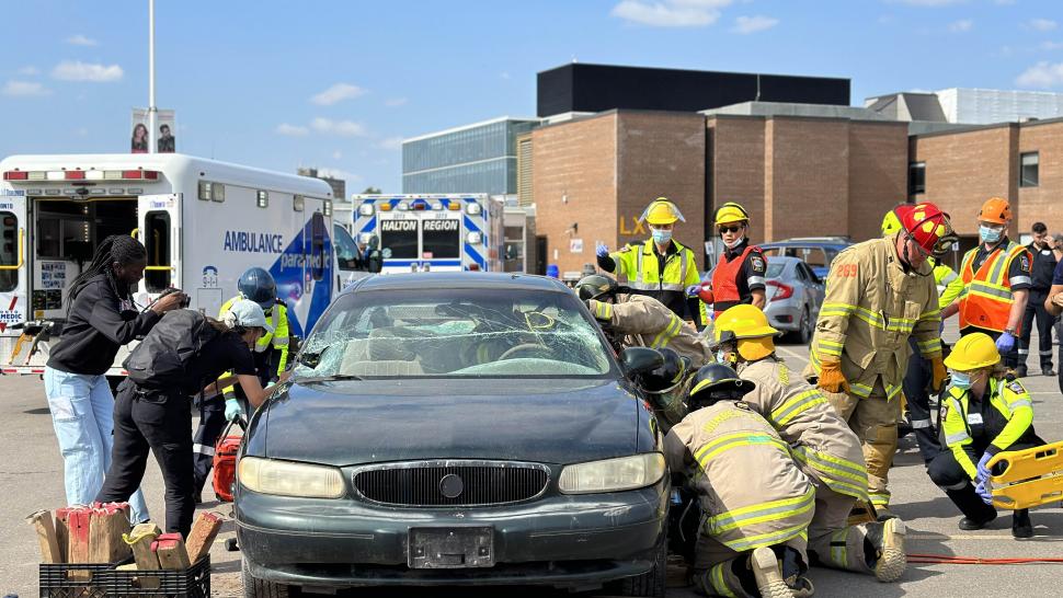 Students wearing firefighter gear work to remove a simulated patient from a vehicle.