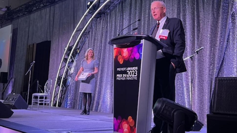 A person speaks into a microphone while standing at a podium that reads Premier’s Awards 2023.