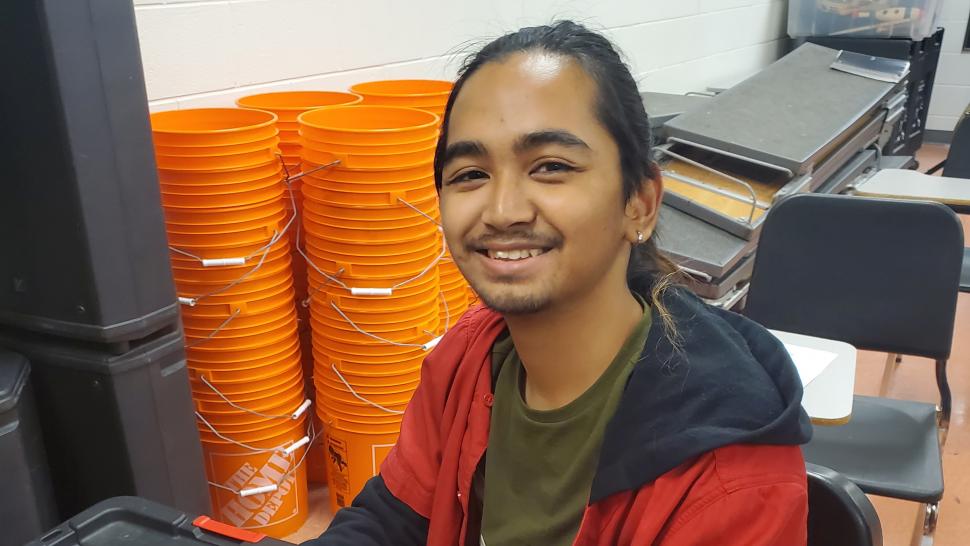 A smiling person sits at a laptop computer.