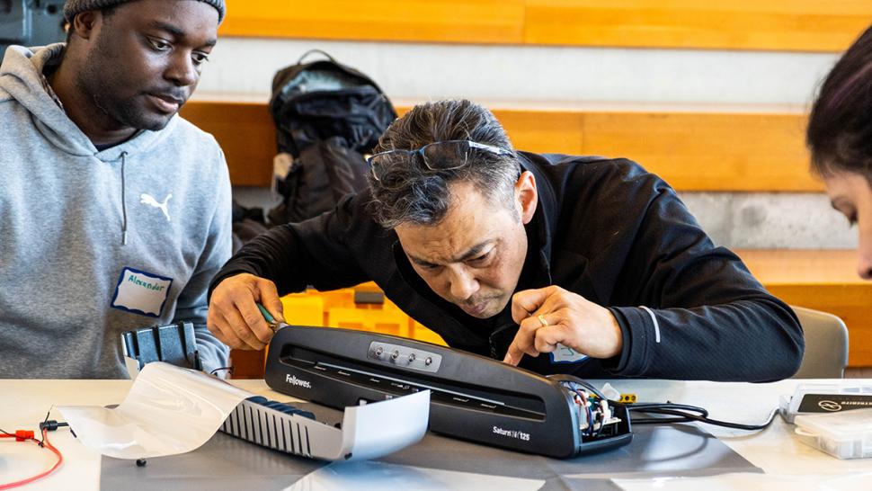 Humber Polytechnic held its first ever Repair Café over two days in April. A person is repairing an electronic device as others watch.