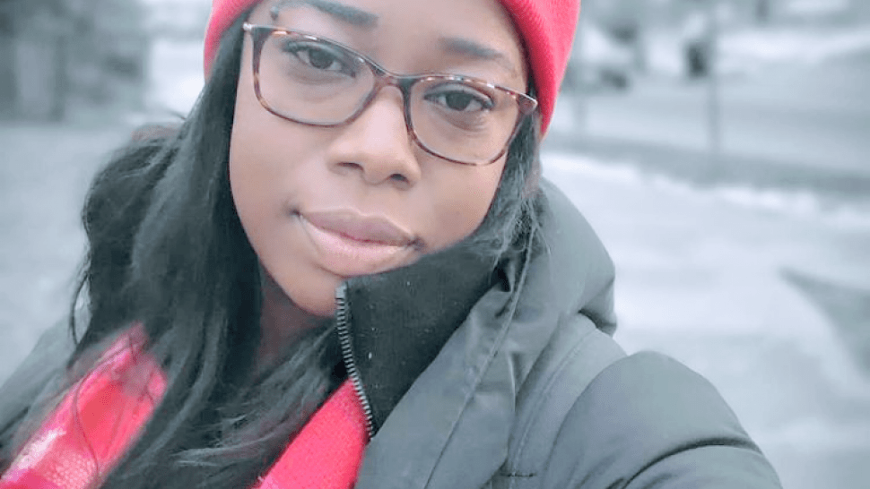 Meshanda Phillips smiles softly at the camera, wearing a pink hat and scarf and puffy jacket on a winter sidewalk