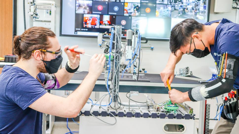 Two students use tools to work on a mechanical device.