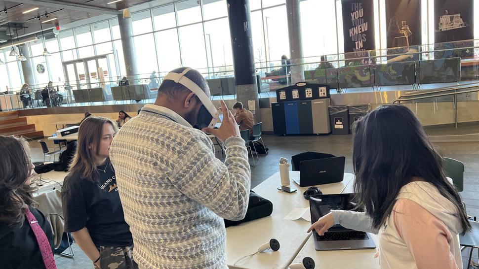 Humber Polytechnic students and faculty took part in a hackathon exploring how spatial technology (such as virtual and augmented reality) and AI can support aging populations. A person is wearing a virtual reality helmet as other people watch.