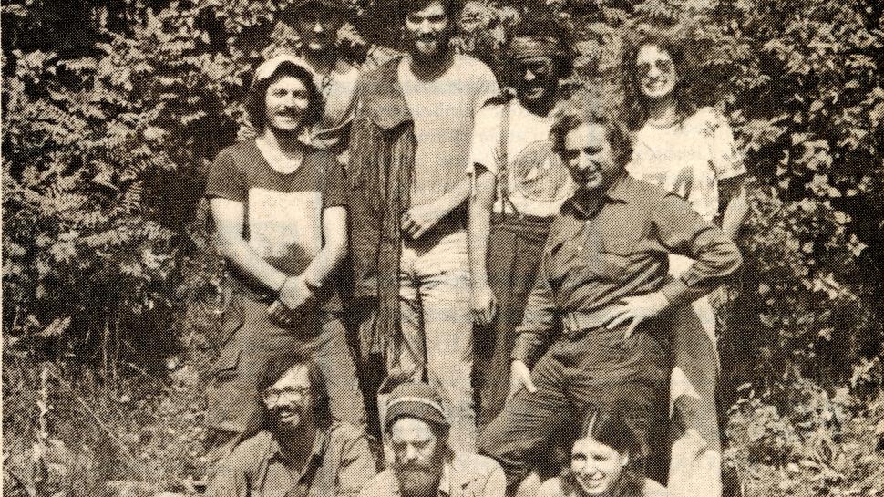 A group of people stand outside a forest and there are two dogs with them.