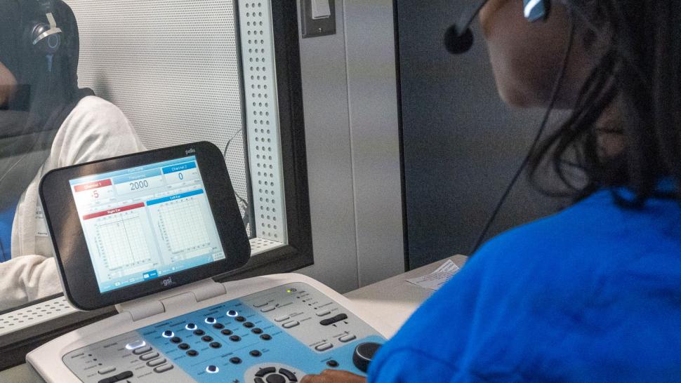 The Hearing Clinic at North Campus is staffed by students in their third semester of the Hearing Instrument Specialist program. A person operates a machine while another person wearing headphones sit in a booth.