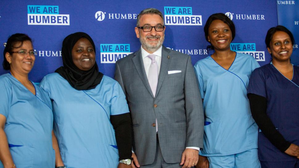 Five people pose for a photo in front of a backdrop that reads We Are Humber. Four of the people are wearing medical uniforms.