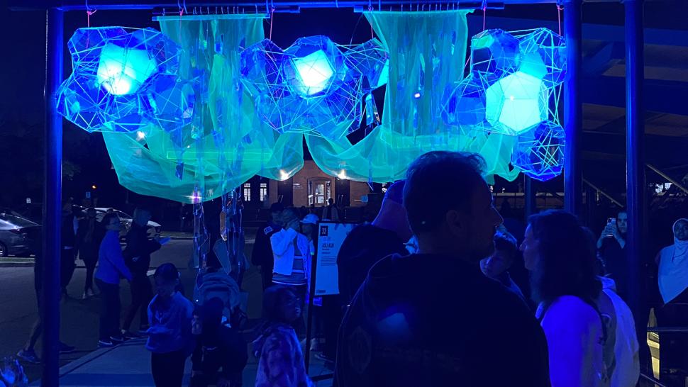 People walk past a florescent art project.