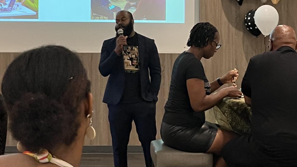 The Black Grad is organized by Black Student Support and Engagement and is an opportunity for the Black community to connect and share their post-secondary experiences. A person speaks into a microphone as others sitting at tables listen.