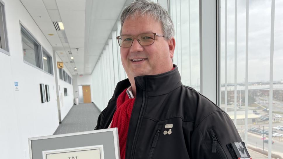 Mark Cameron stands in a hallway at Humber College and poses for a photo holding his 2022 Premier’s Award.