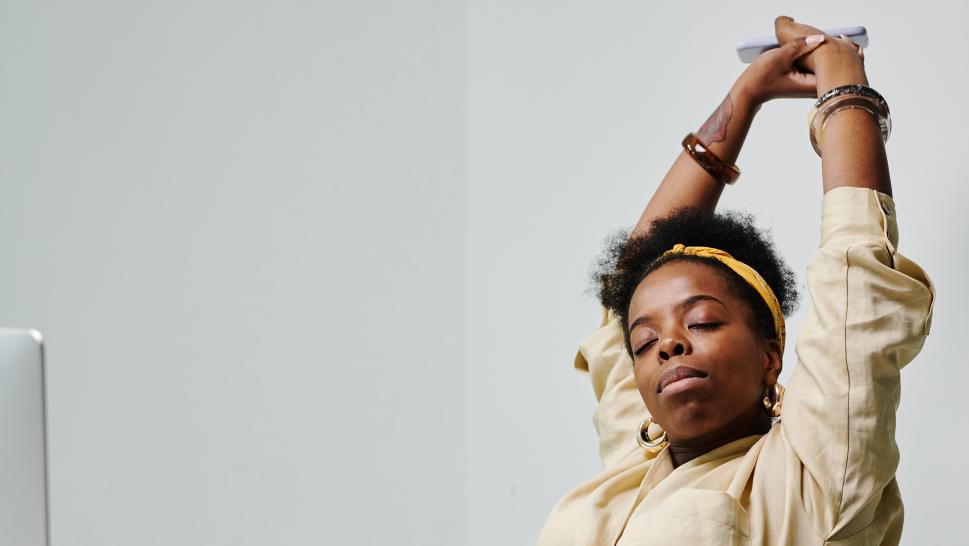 A person sitting at a desk has their hands and arms above their head as they stretch.