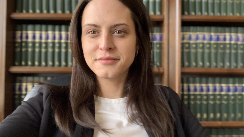 Paralegal Studies student Caitlyn McCann gazes into the camera, smiling slightly, in front of a bookshelf wearing a grey blazer