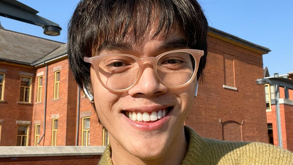 A smiling person poses for a photo in front of brick buildings.