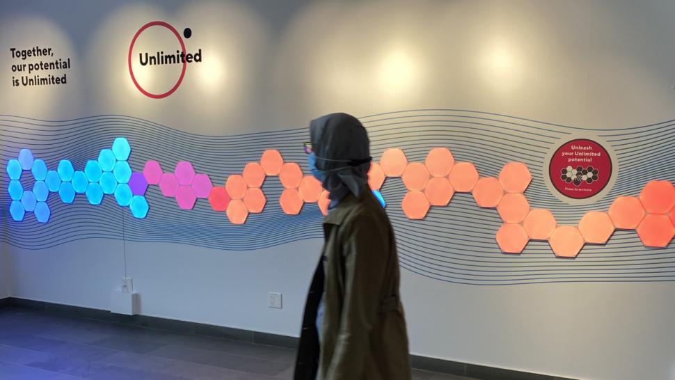 A person walks past a mural consisting of a series of brightly lit hexagons of different colours.