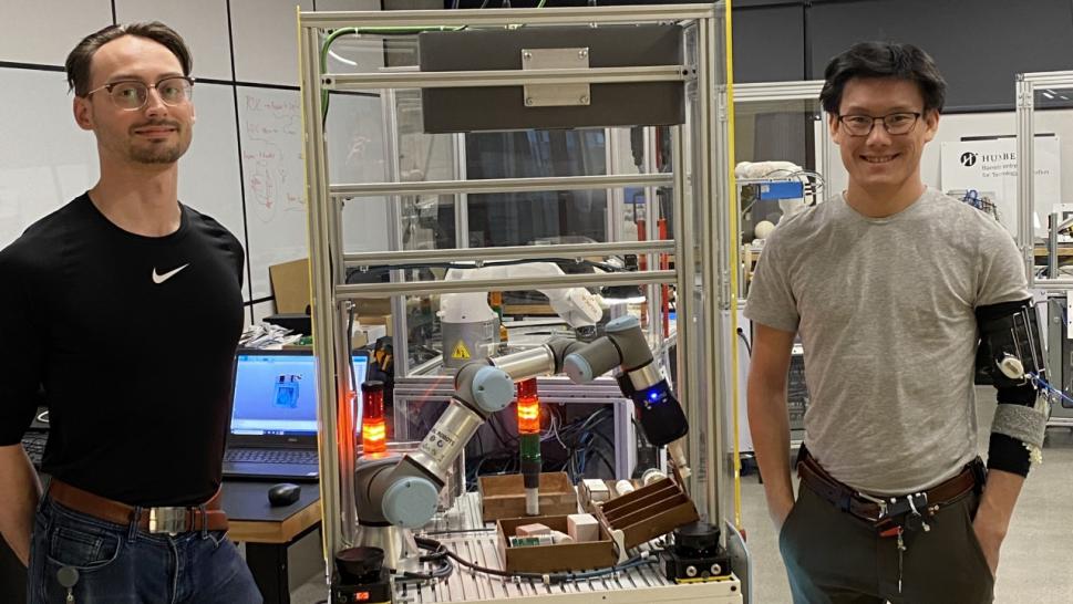 Two people stand on opposite sides of a robotic device that can sort recyclable items.