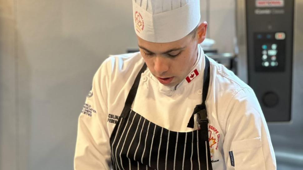 A person wearing a chef’s uniform preps food in a kitchen.