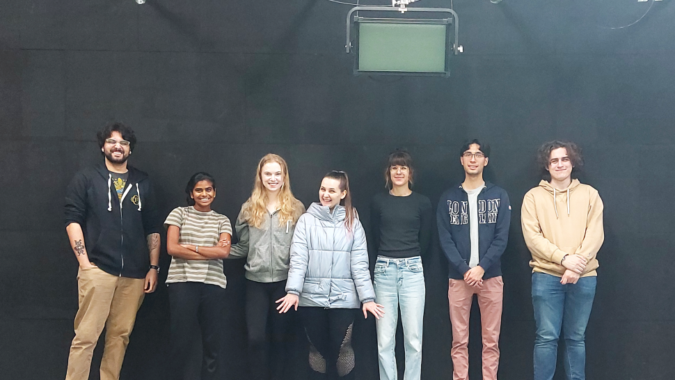 A group of seven people smile as they stand in front of a black backdrop.