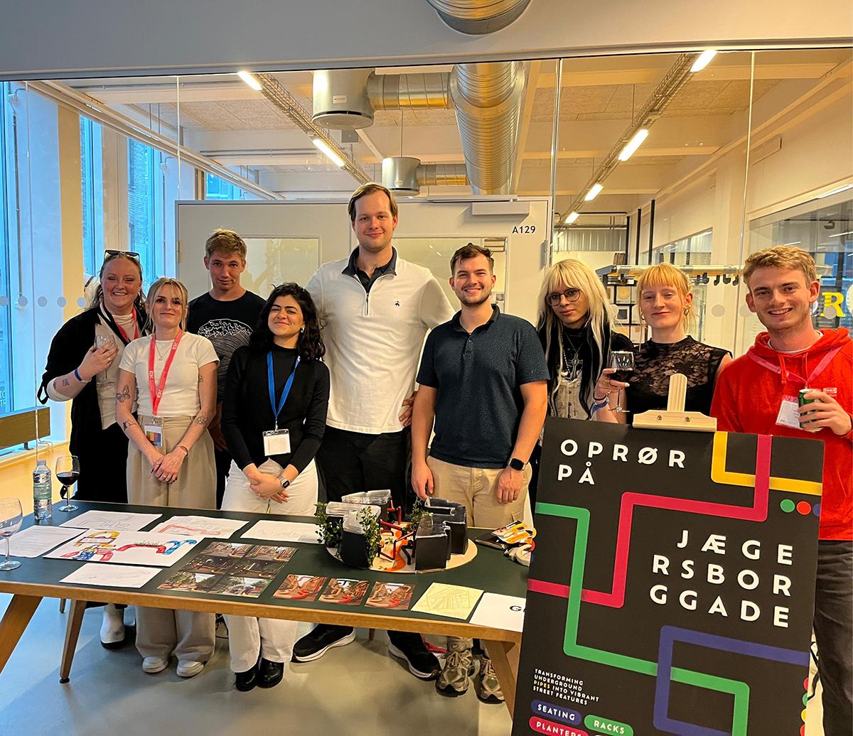 A group of people stand in front of a table that has information and displays on it for a presentation.