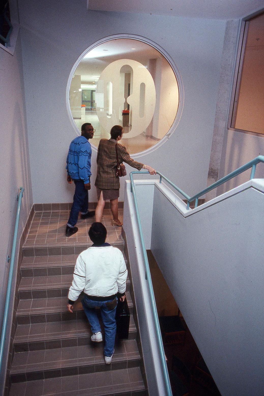 People walk up a flight of stairs past the original Humber College logo.