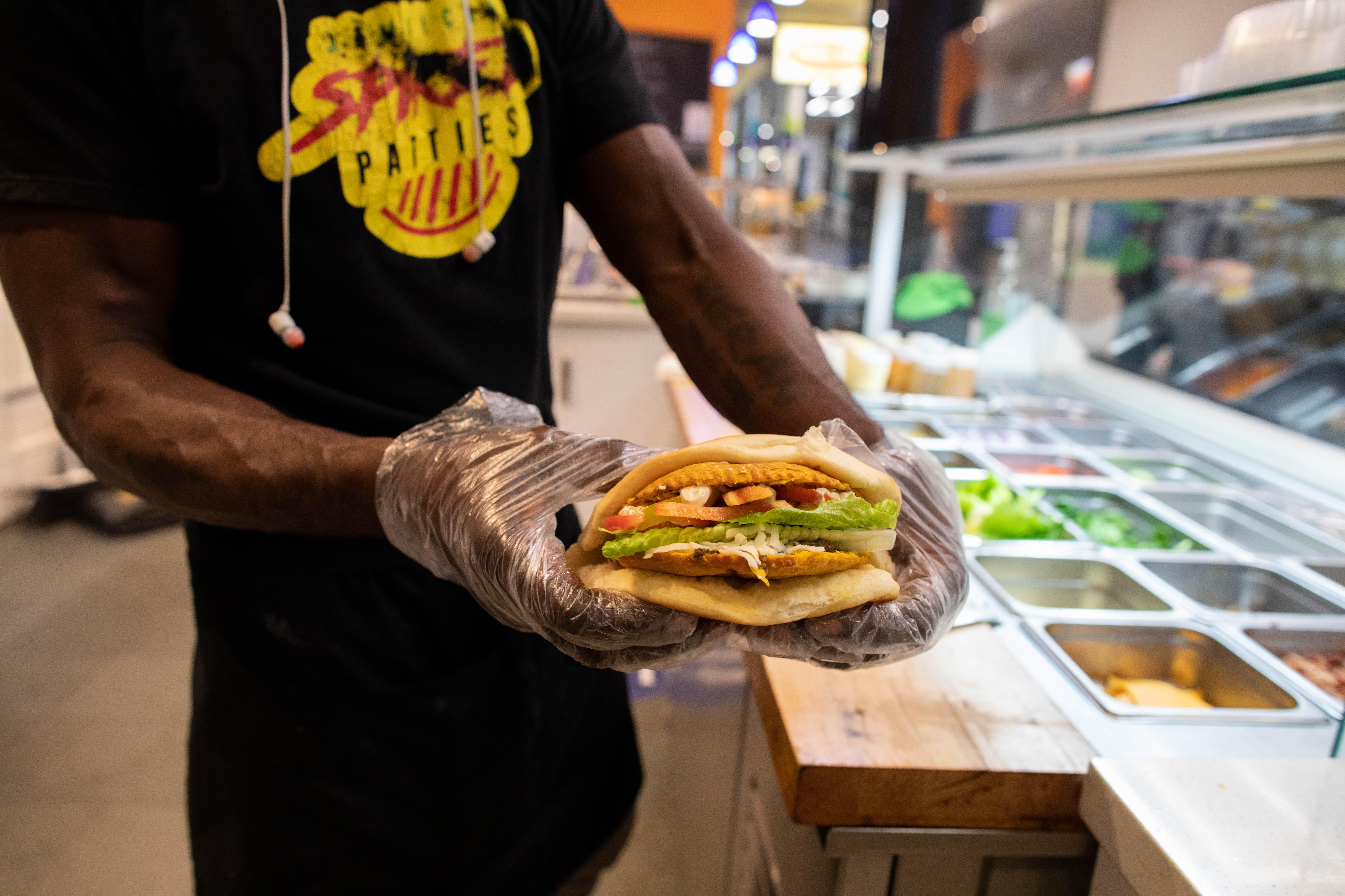 A person holds a Jamaican patty served on coco bread that has been cut in half.