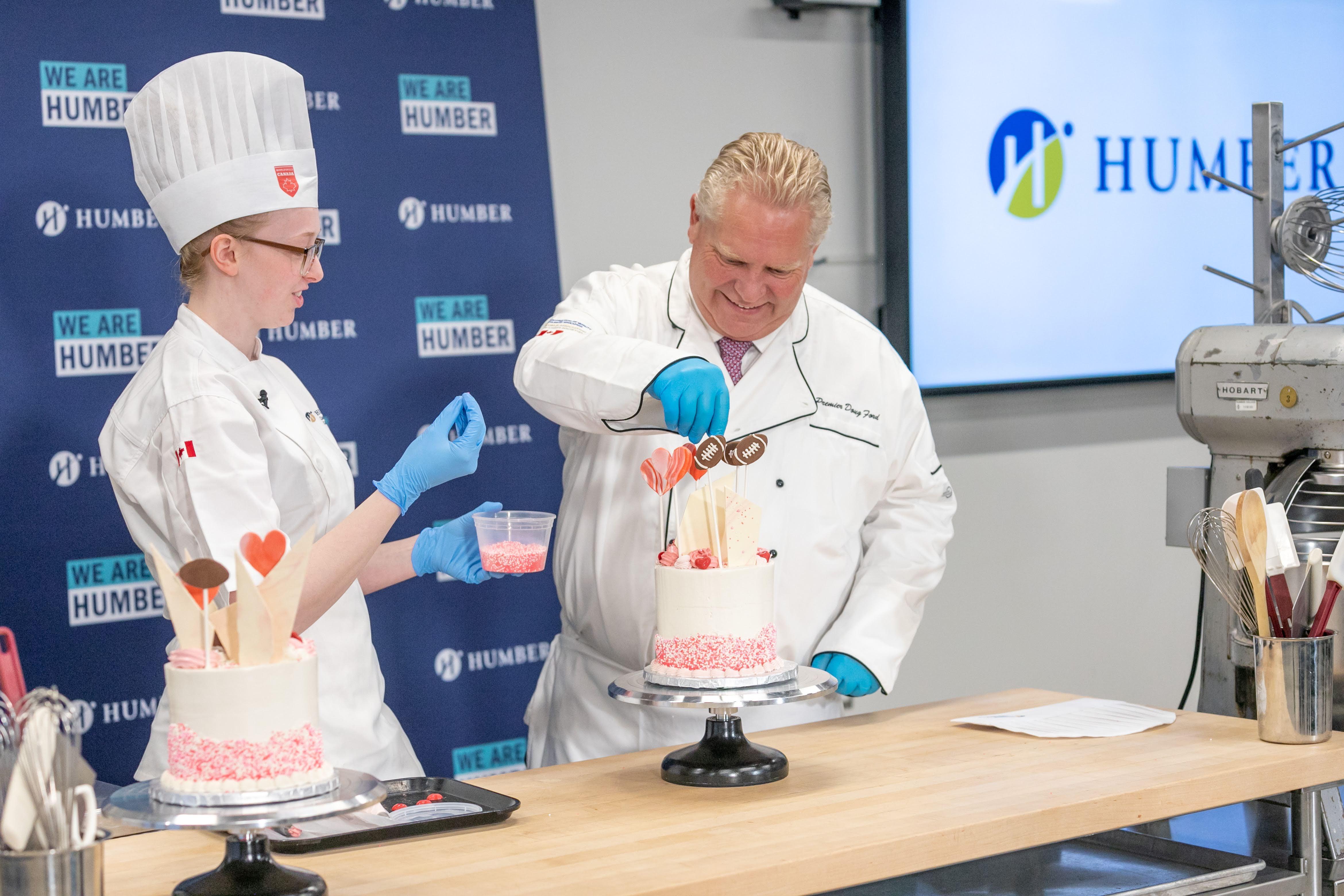  Premier Doug Ford wearing a chef’s outfit decorates a cake with the help of Humber graduate Emma Kilgannon.