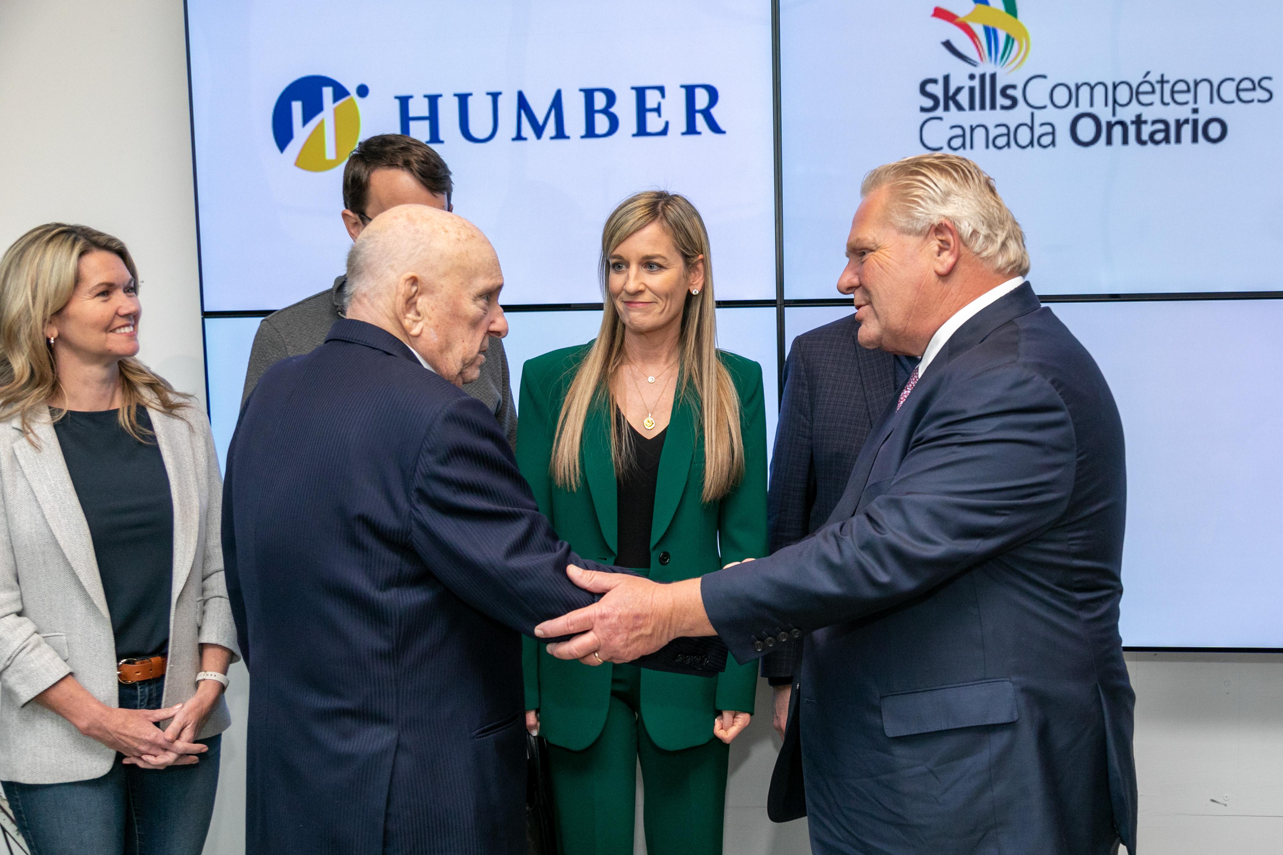 Premier Doug Ford shakes a person’s hand while Judy Schulich and others watch.