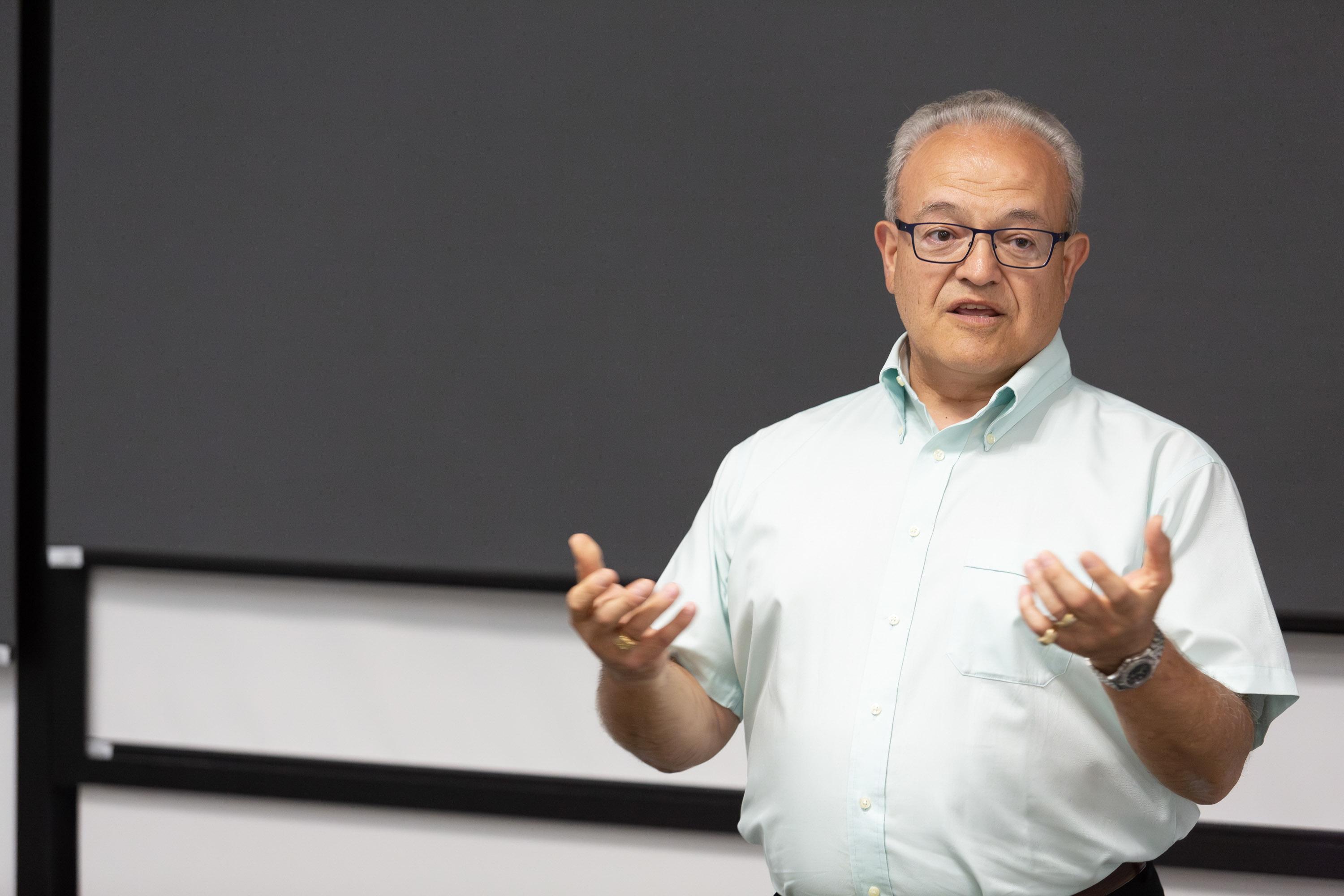 A person stands in front of a blackboard while speaking to an audience.