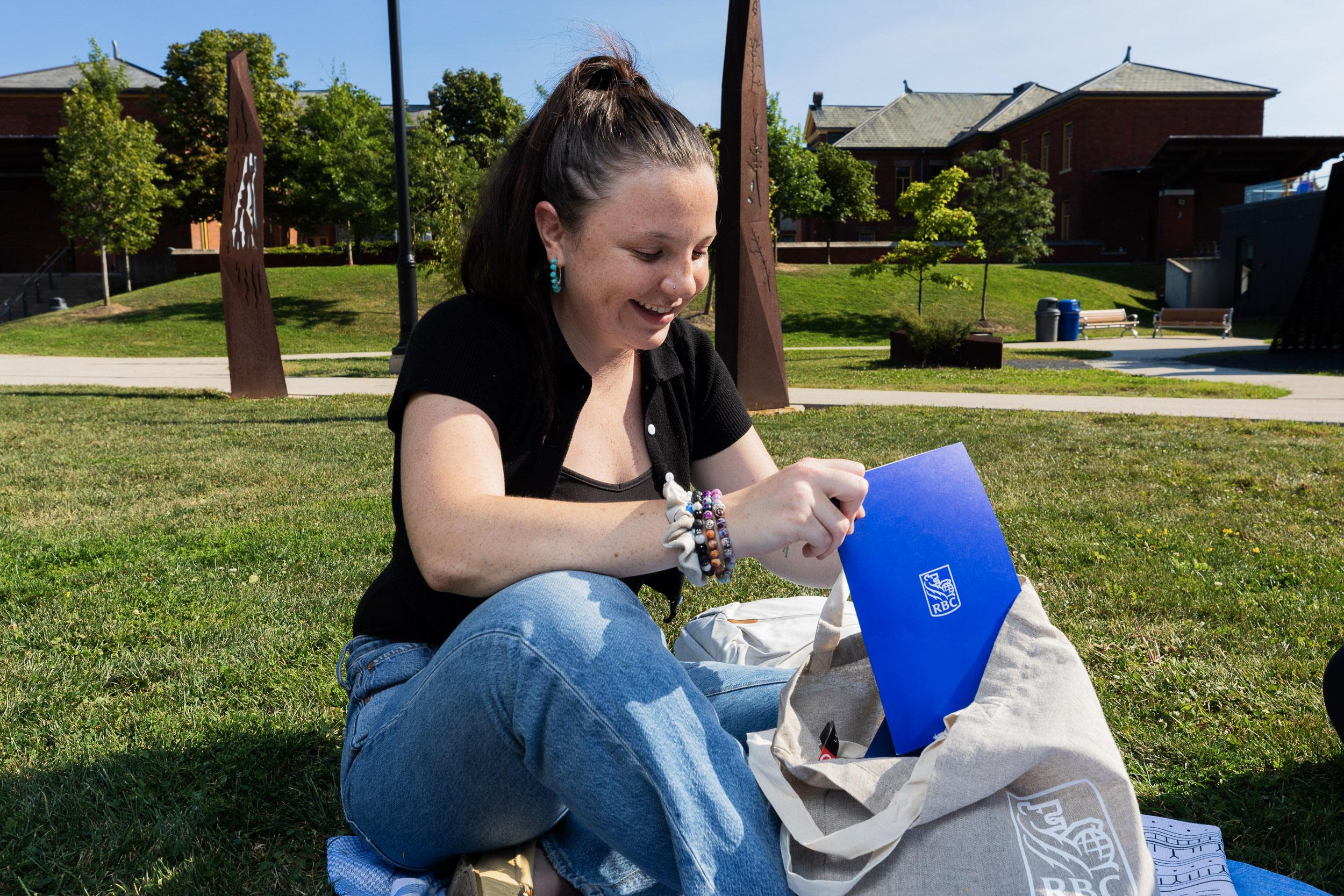 A smiling person pulls a blue folder with the RBC logo on it from a bag with the RBC logo on it. 