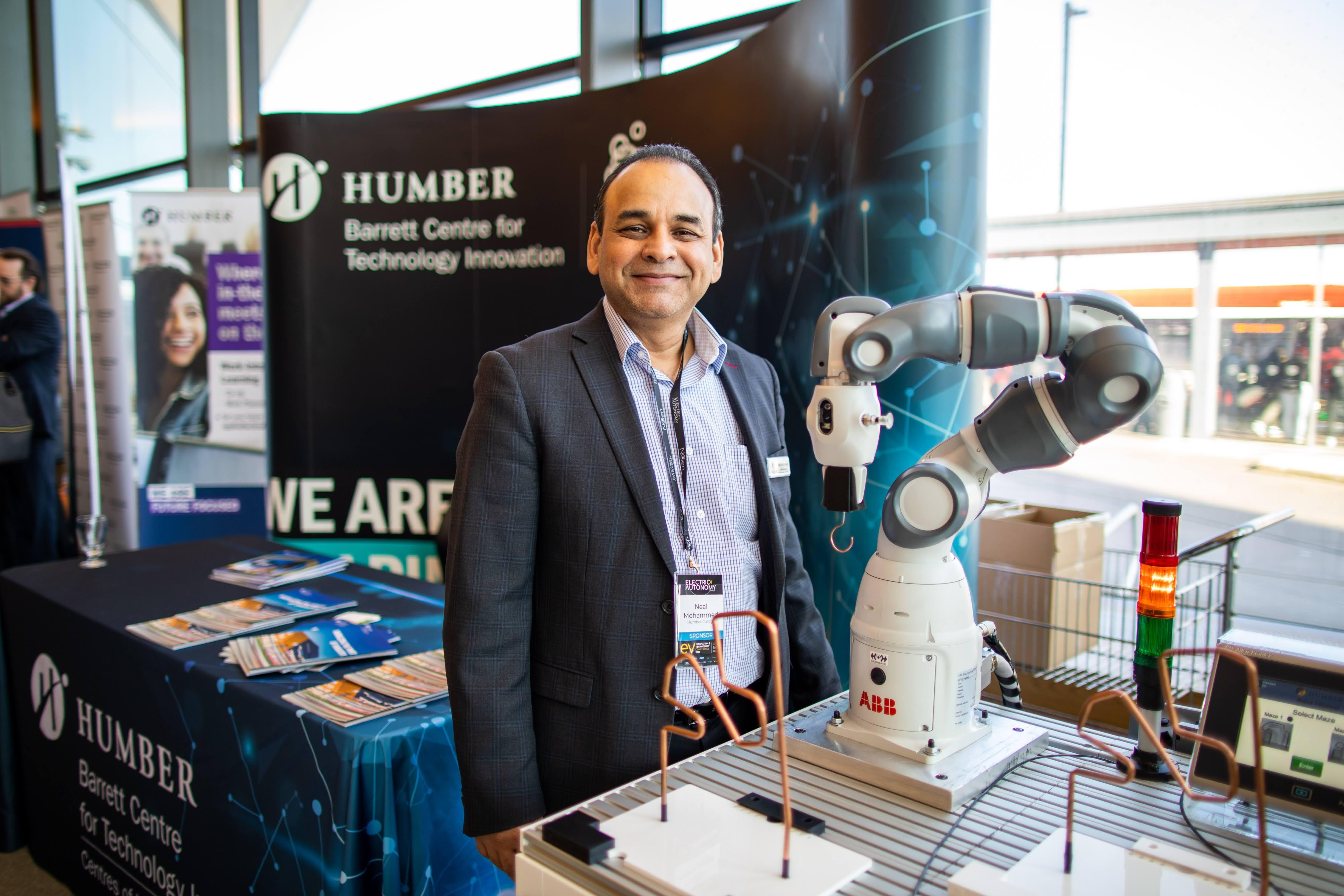Neal Mohammed stands in front of a robot. Behind him is a sign that reads Barrett Centre for Technology Innovation.