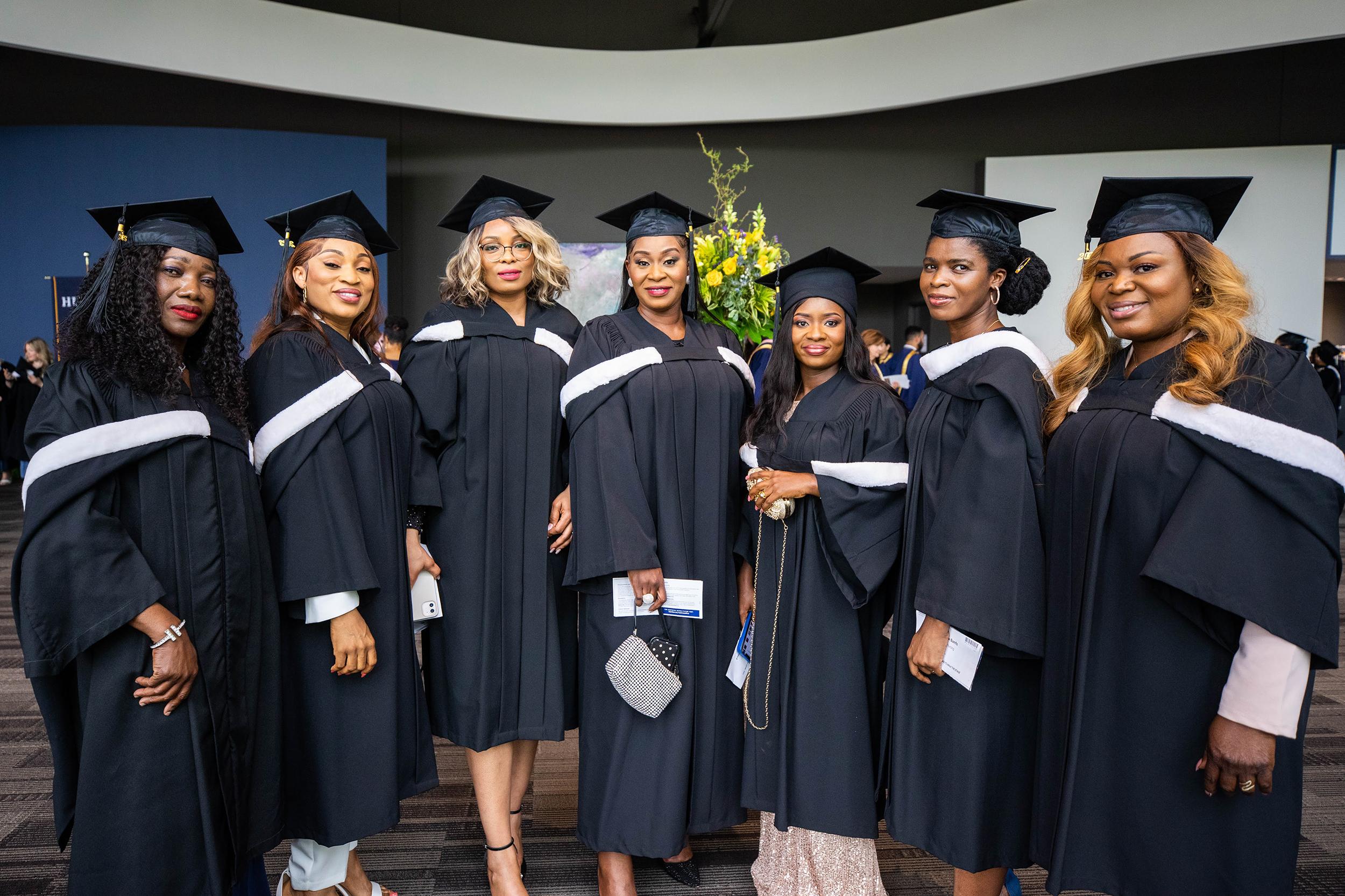 Seven people wearing graduation robes and caps pose for a photo.