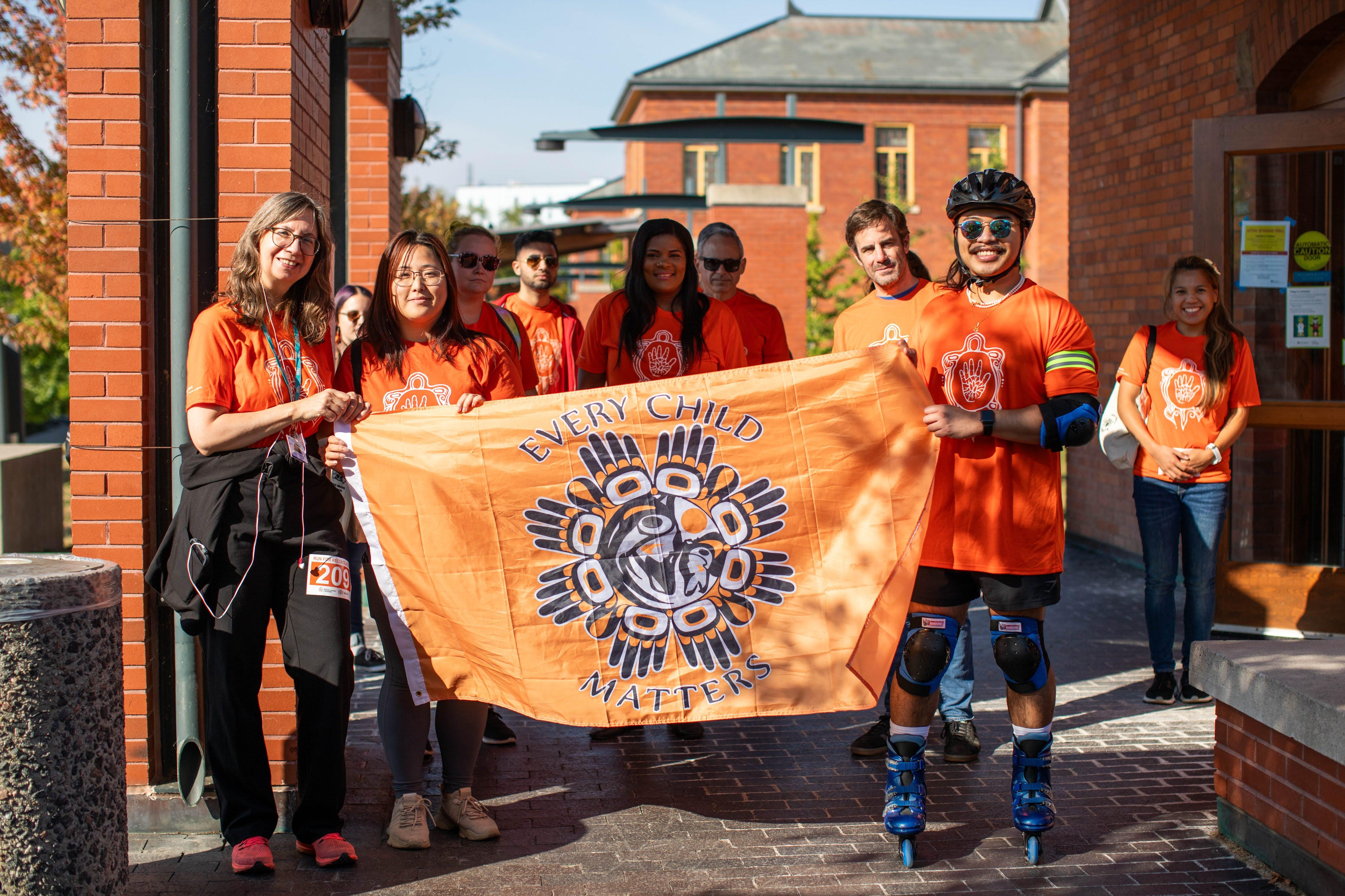 People wearing orange shirts hold up a sign reading Every Child Matters.