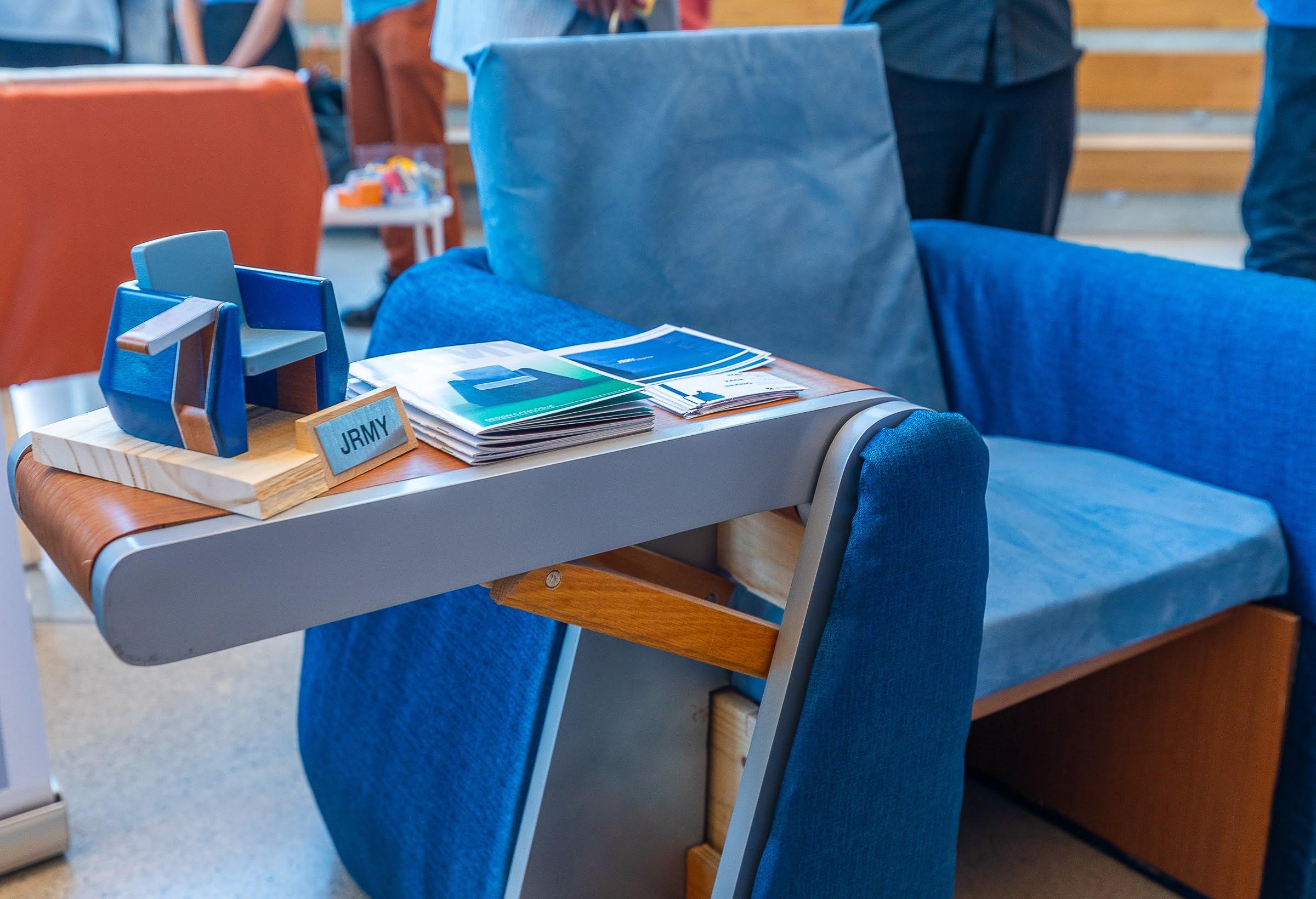 A blue chair that has a miniature replica of it sitting on its armrest along with pamphlets.