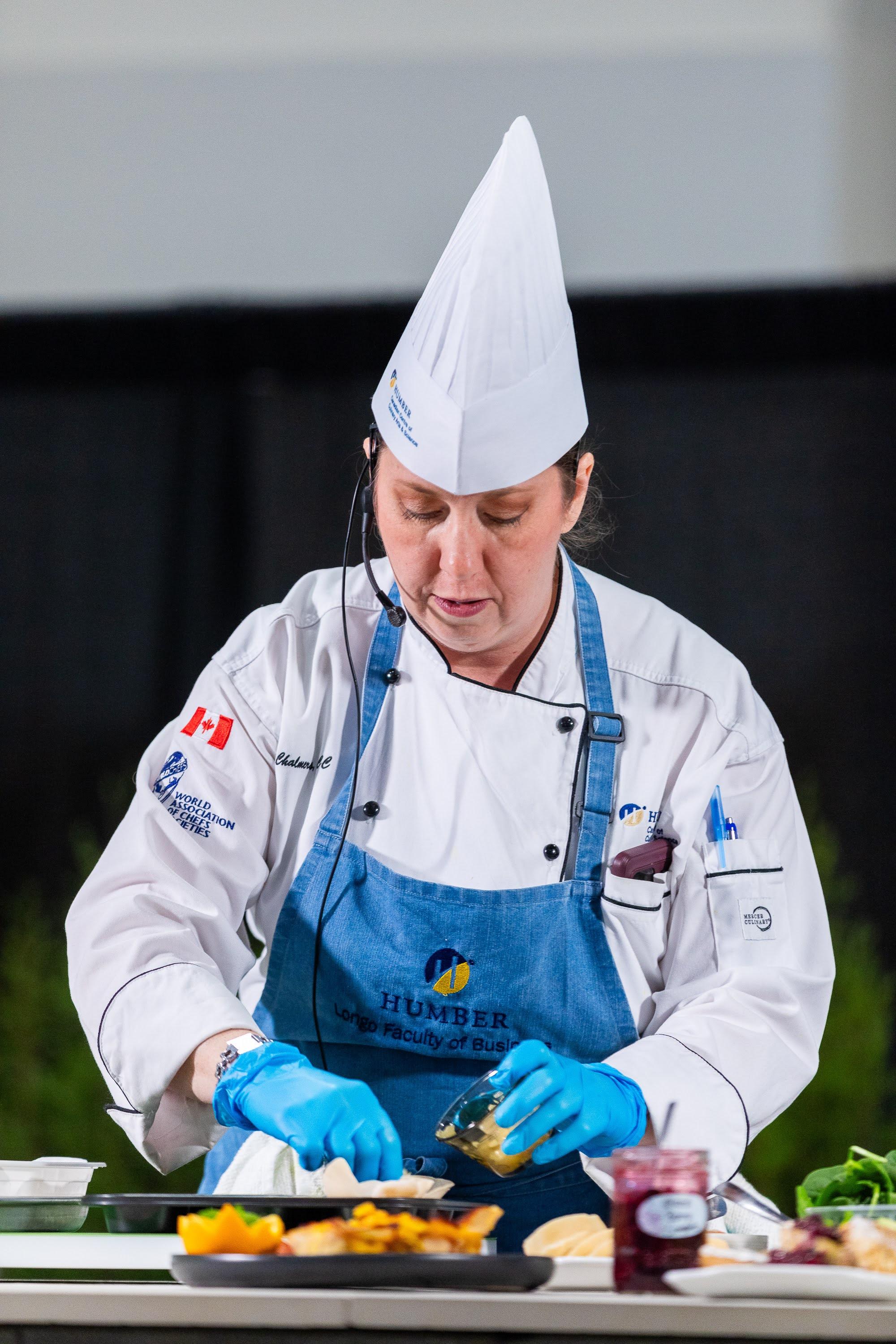 A person wearing a chef uniform puts food on a plate.