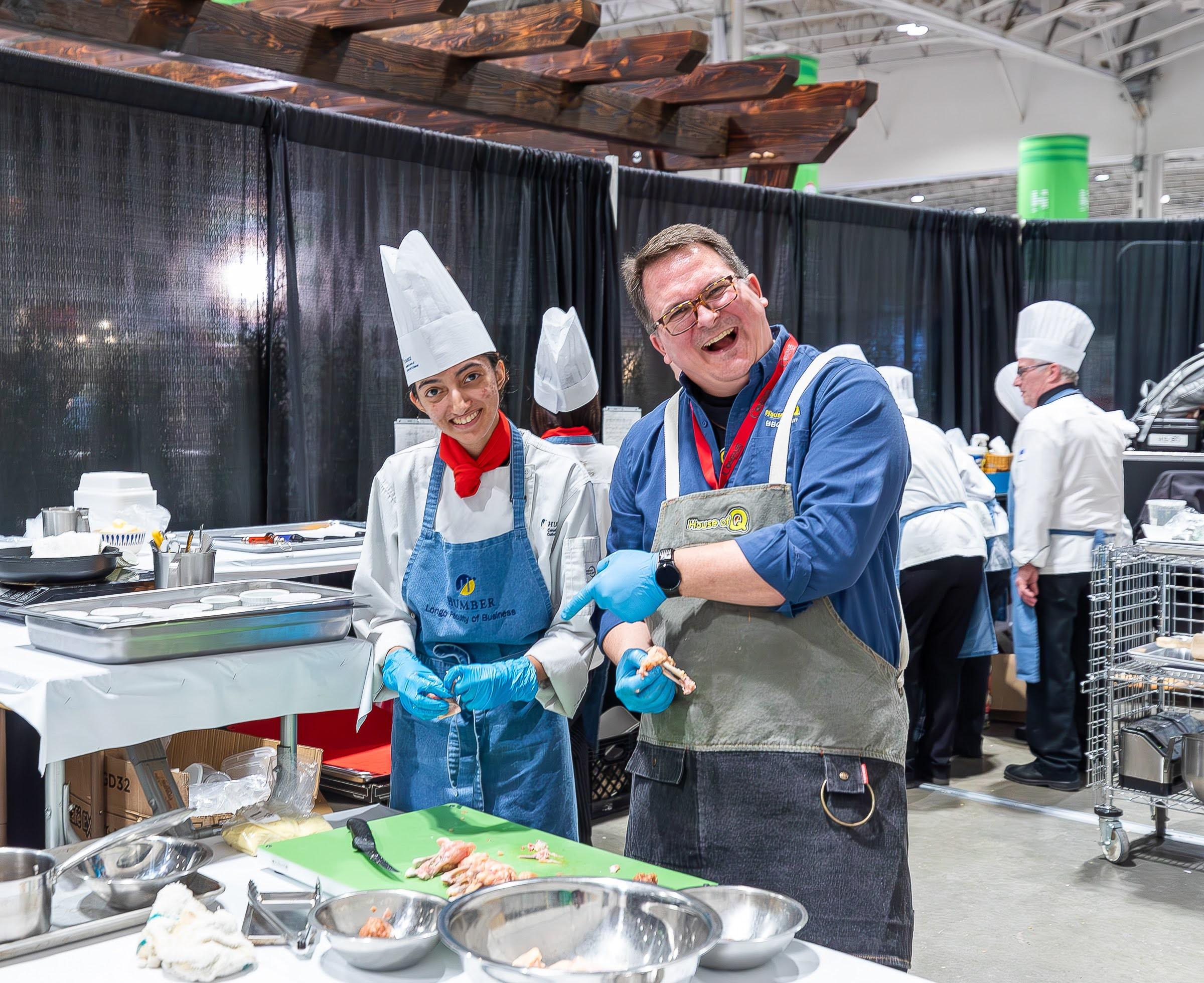 Two people prepare food to be cooked. One is wearing an apron with a Humber logo on it.