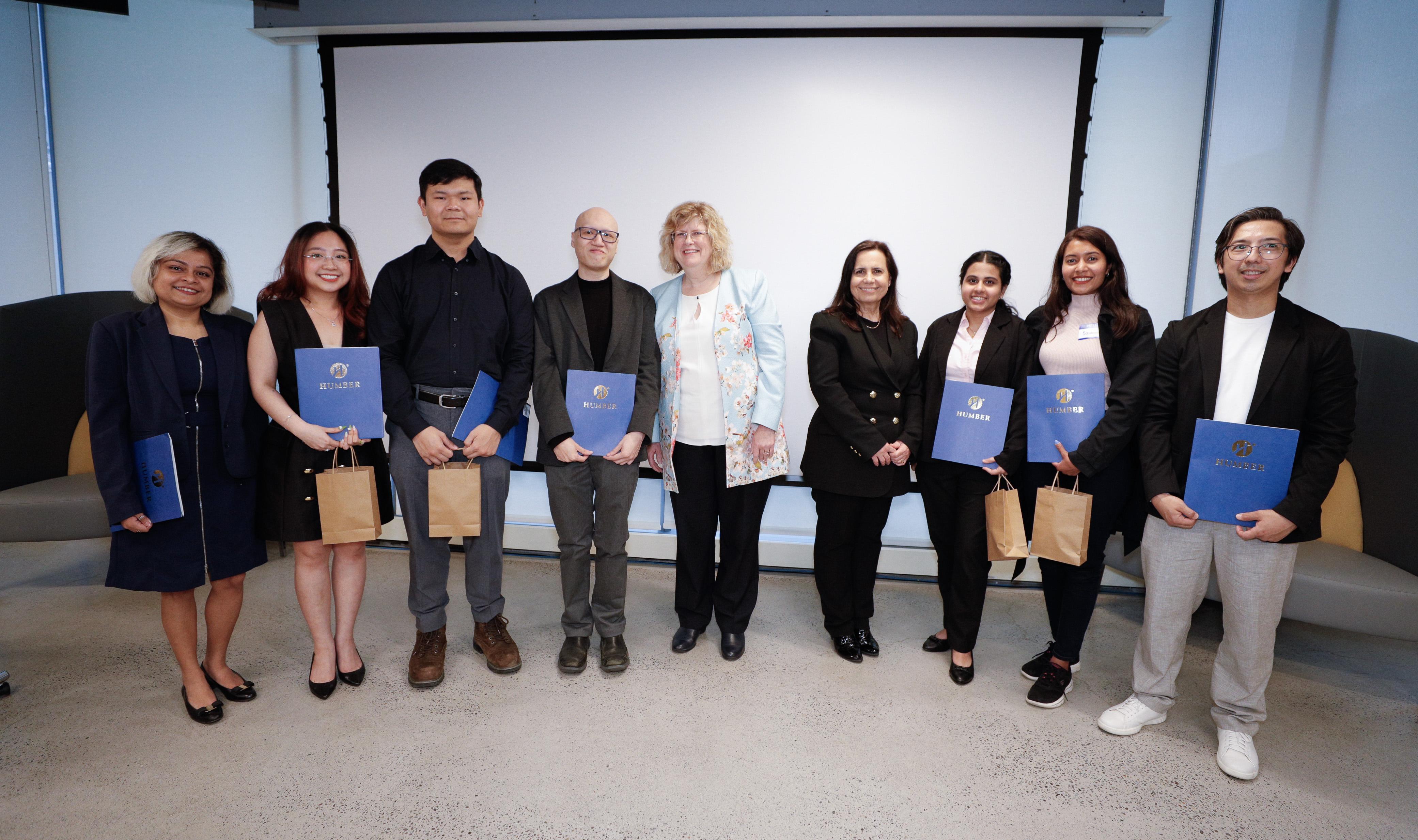 A group of smiling people stand together holding blue awards.