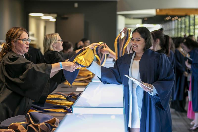 A person wearing a graduation gown is handed a sash.