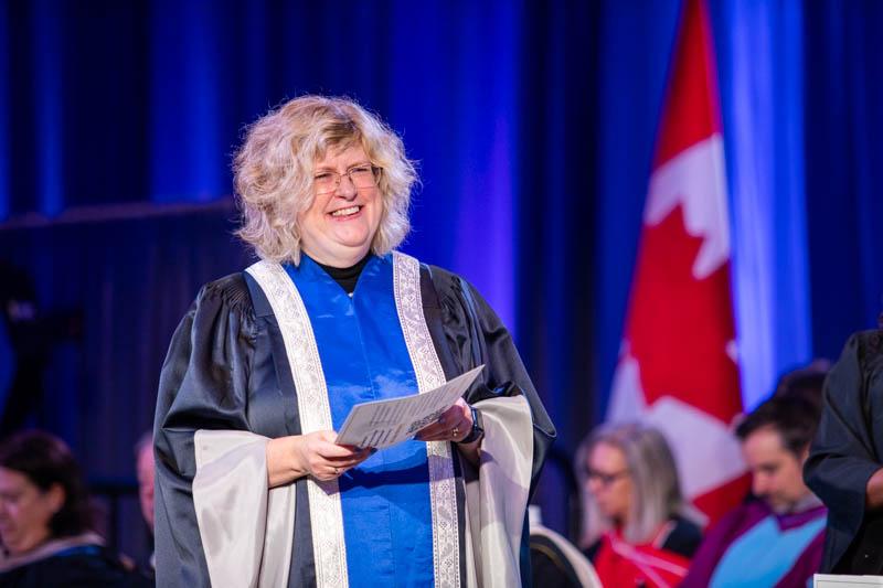 A person wearing a graduation robe smiles.