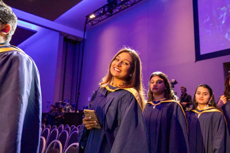 A person wearing a graduation robe smiles.