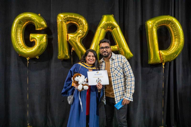 Two people stand beneath balloons that spell out the word Grad.