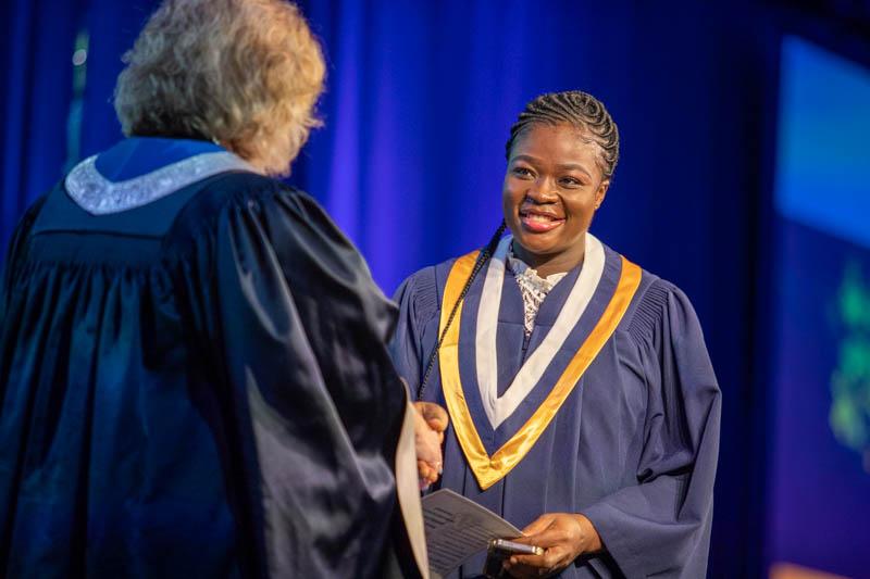 A person wearing graduation robes accepts their credential from another person.