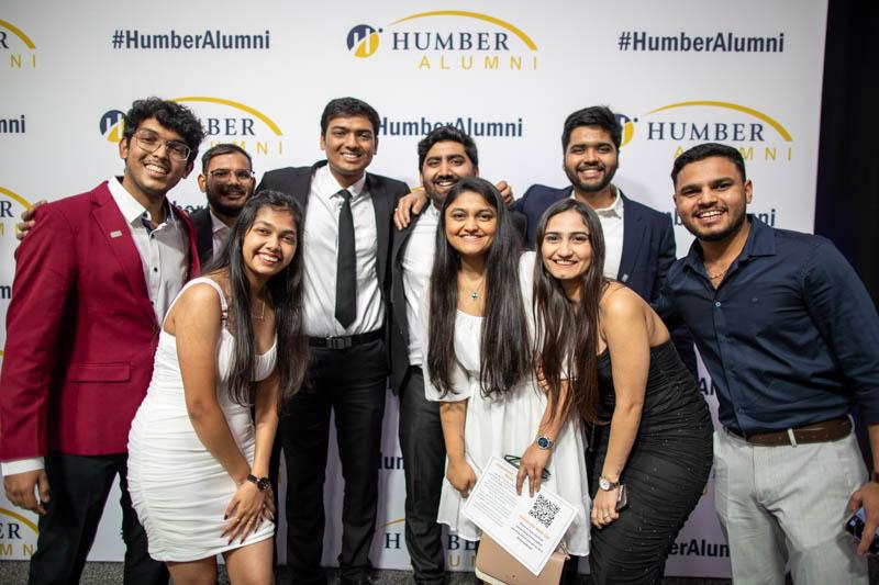 A group of people pose for a photo in front of a banner that reads Humber Alumni.