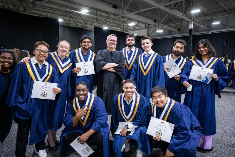 A group of people wearing graduation robes are holding up pieces of paper with Humber written on them.