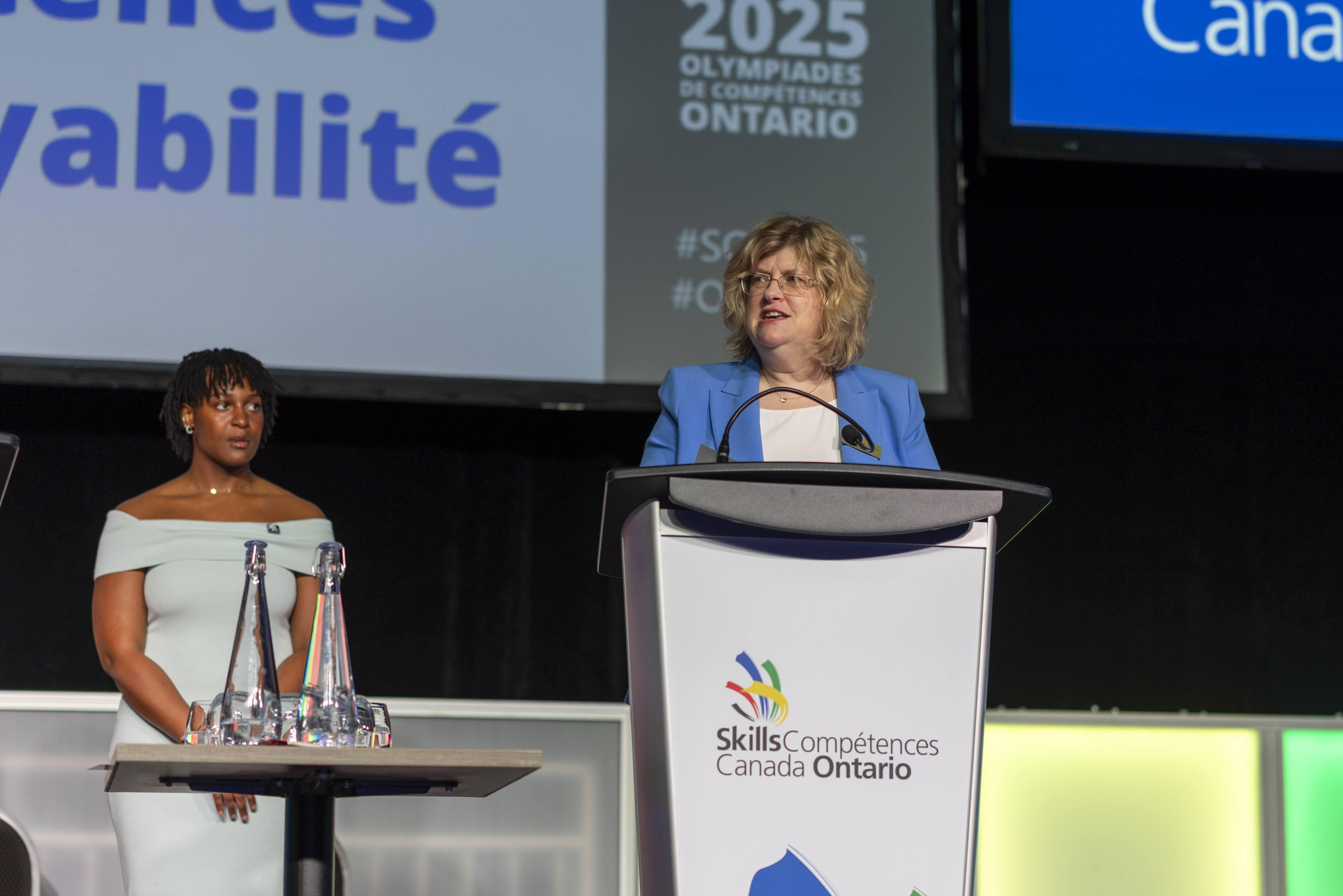 A person speaks into a microphone while standing at a podium on a stage.